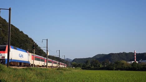 Railway-train-passing-by-a-agricultural-land-with-mountains-and-forest-in-the-background