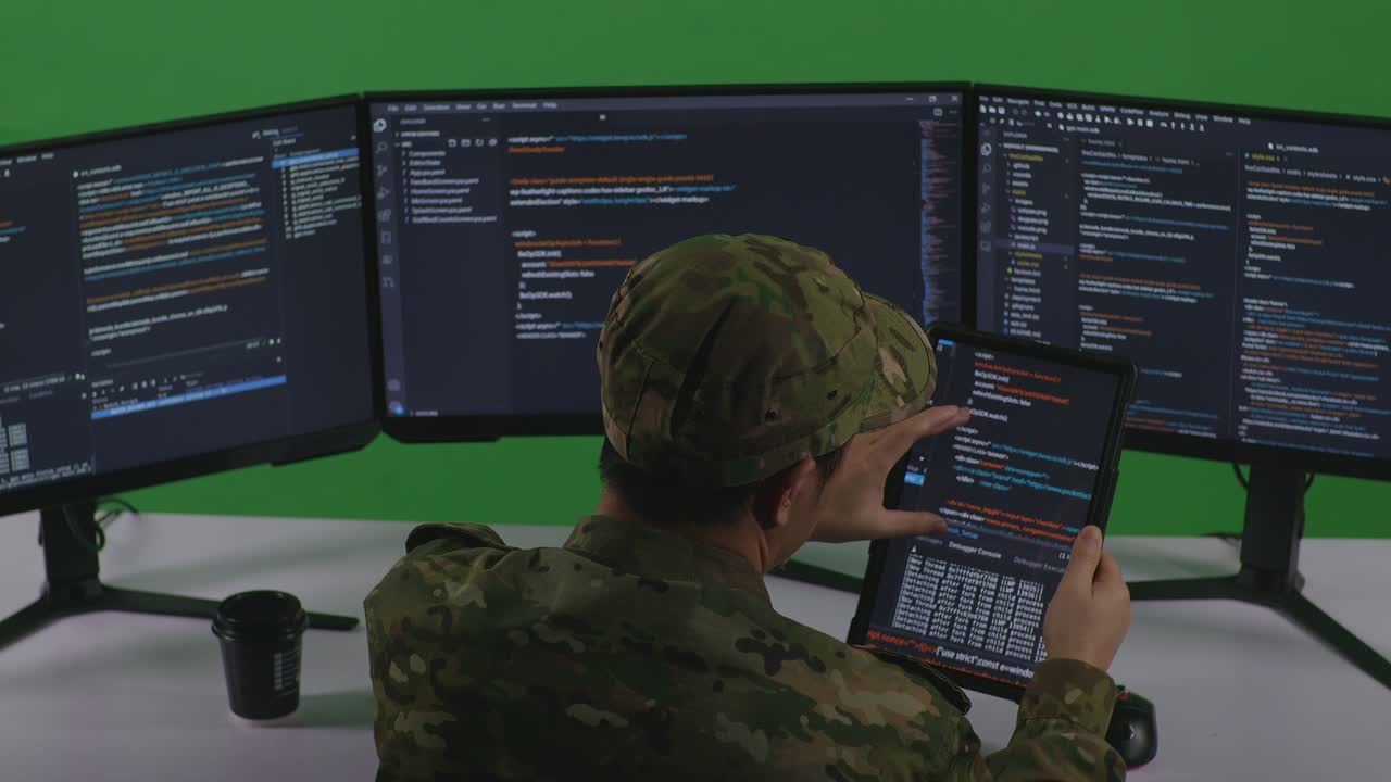 Back View Of Asian Man Soldier Developer Working With Tablet While Write Code With Multiple Computer Screens In Green Screen Studio