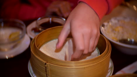 girl taking a pancake wrap from a bamboo bowl in a chinese restaurant