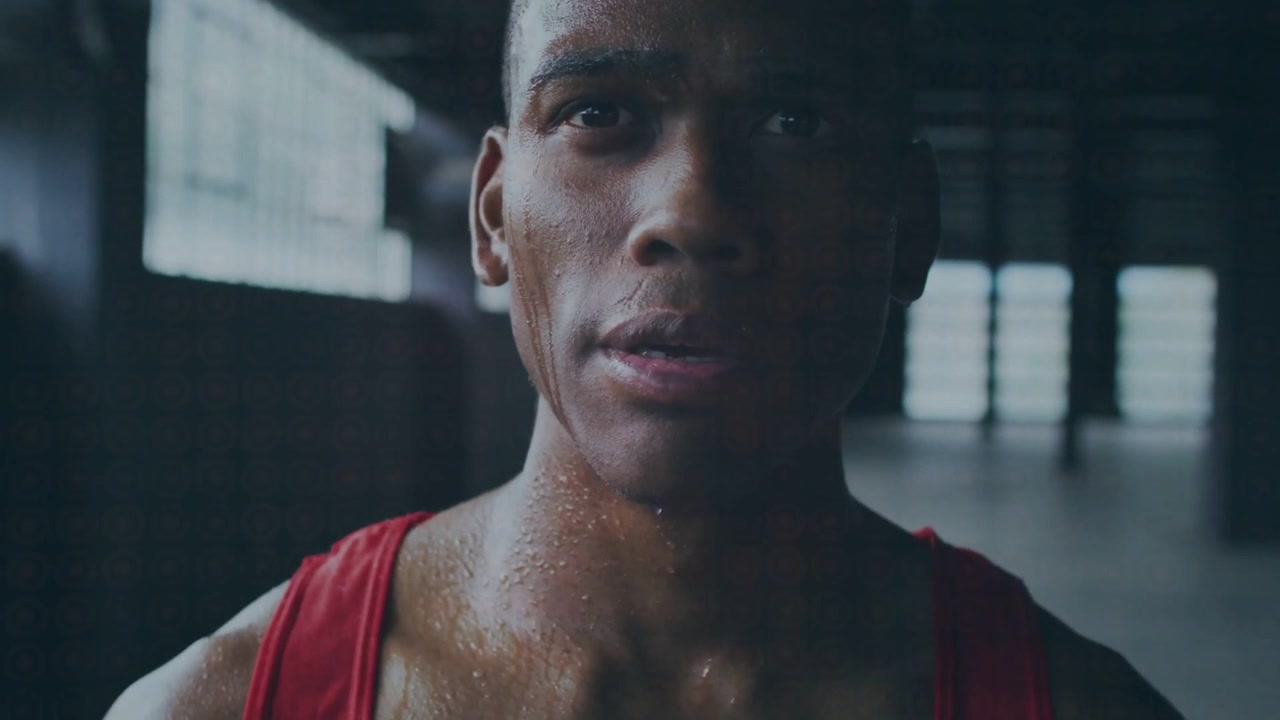 Camera pulling back showing athlete training in gym, red tank top sweat glistening, scar emerging