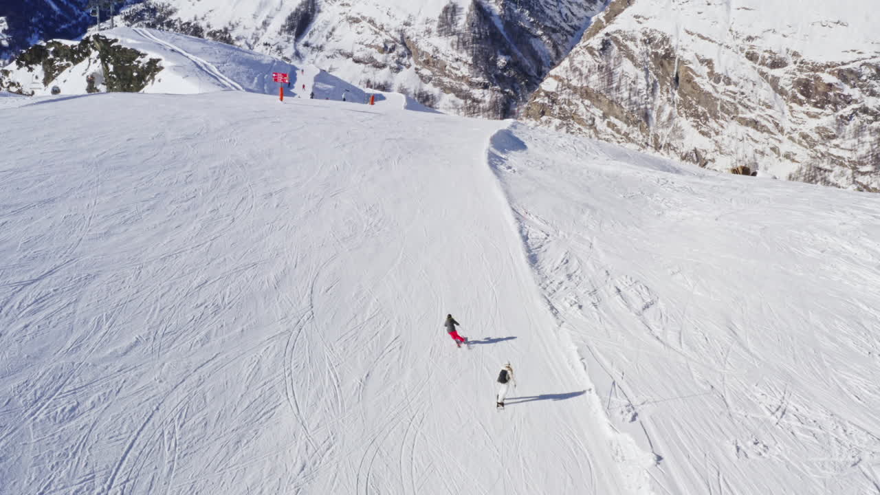 Aerial Following Shot of Professional Skier and Snowboarder going Down the Snowy Slope