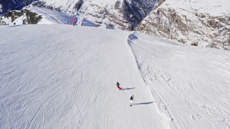 aerial following shot of professional skier and snowboarder going down the snowy slope