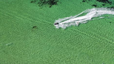 aerial view, jetski watercraft towing skier in clear shallow ocean water of west australia, top down tracking drone shot