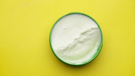 crema en un frasco verde sobre un fondo amarillo