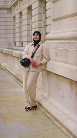 Vertical-Video-Full-Length-Portrait-Of-Muslim-Businesswoman-Wearing-Hijab-And-Modern-Business-Suit-Standing-Outside-City-Office-Buildings