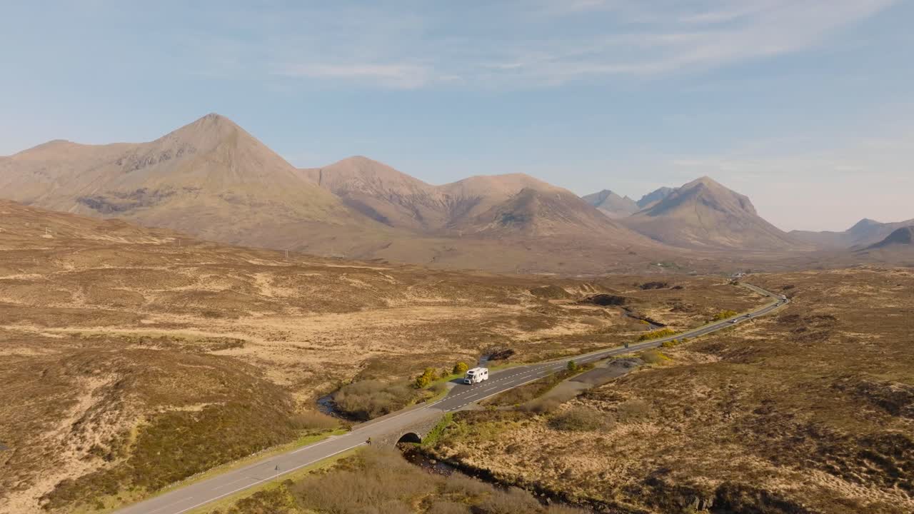 Aerial drone footage of a camper van on mountain road on the Isle of Skye, Scotland. Surrounded by dramatic peaks, scenic valleys, and wild nature