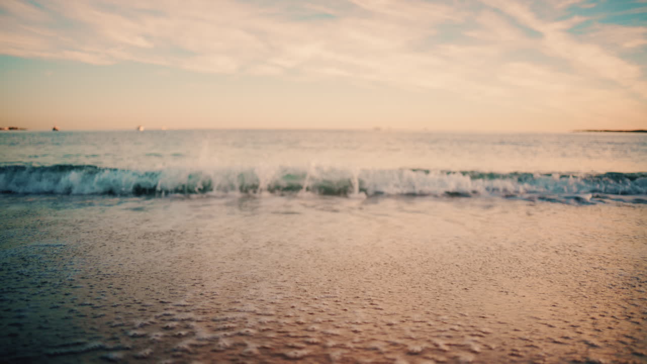 Close up of small ocean waves gently rolling onto the sandy beach at sunset
