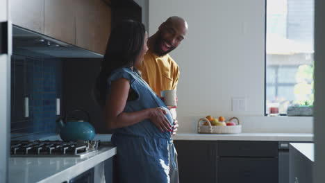 loving hispanic husband with pregnant wife at home in kitchen feeling baby kick together