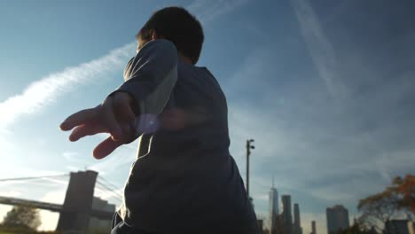 niño corriendo desde el puente de manhattan hacia el atardecer y el puente de brooklyn en el campo de hierba
