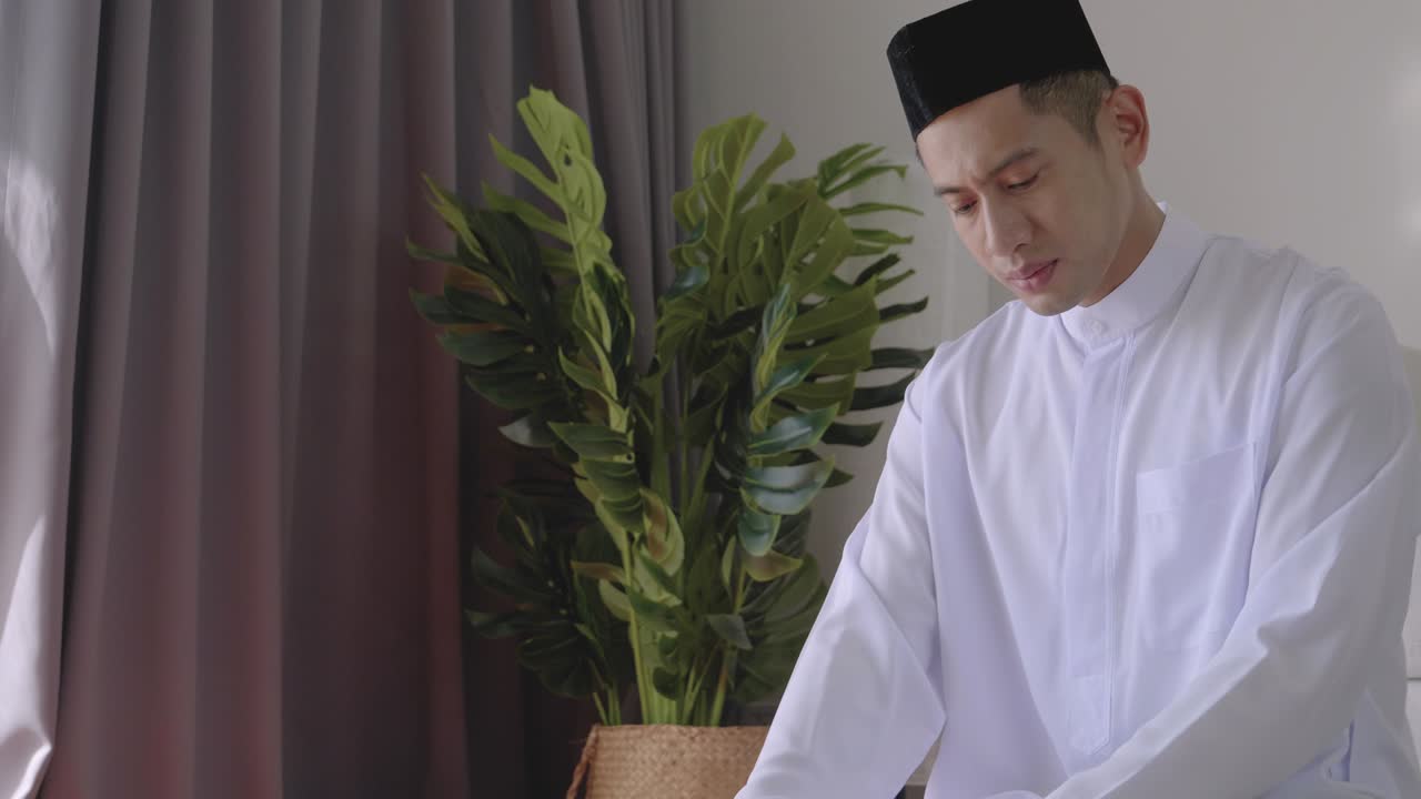 무슬림 남자는 집에 앉아서 책을 읽고 손으로 공중에서 기도합니다.