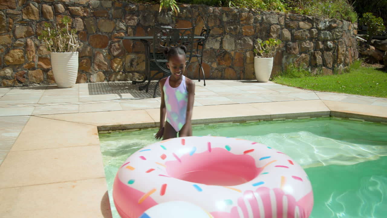 Child joyfully playing in swimming pool with inflatable donut float, enjoying summer