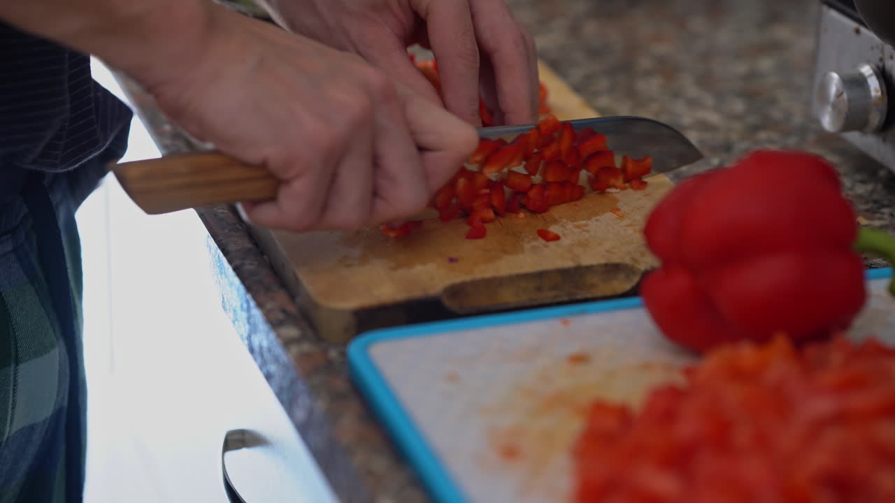 primer plano de la mano del hombre con un cuchillo cortando pimiento rojo fresco en una tabla de madera