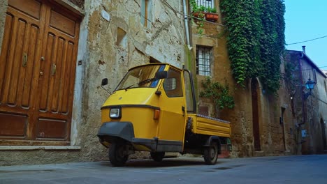 Vehículo-Amarillo-Piaggio-Ape---Vespacar-Estacionado-En-El-Estrecho-Callejón-De-Pitigliano,-Italia