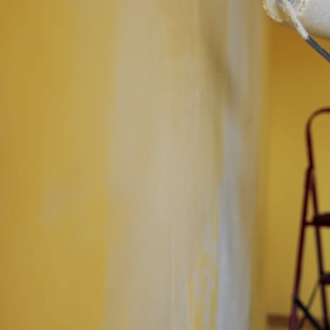 hand with paint roller during room renovation. man moving paint roller with white color on the wall. professional painting services. close-up
