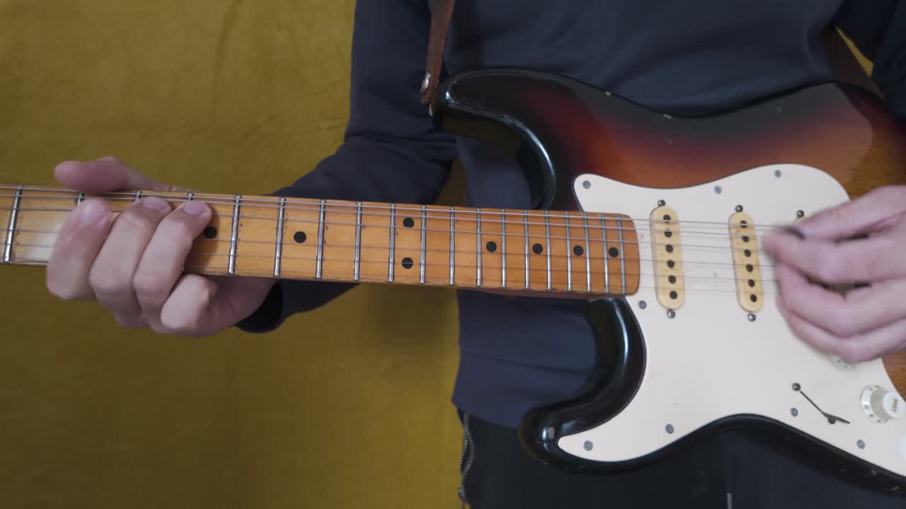 Musician playing a sunburst Fender Stratocaster electric guitar with a maple neck