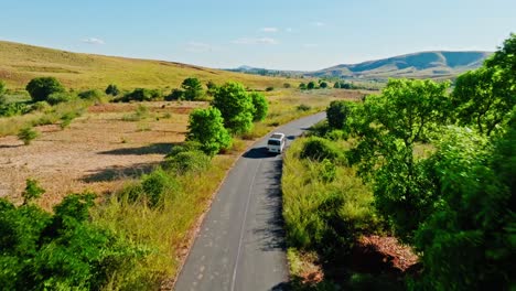 aerial view of a white bus driving along a remote road through grassy highlands and green trees in madagascar. peaceful rural transportation scene under a clear sky.