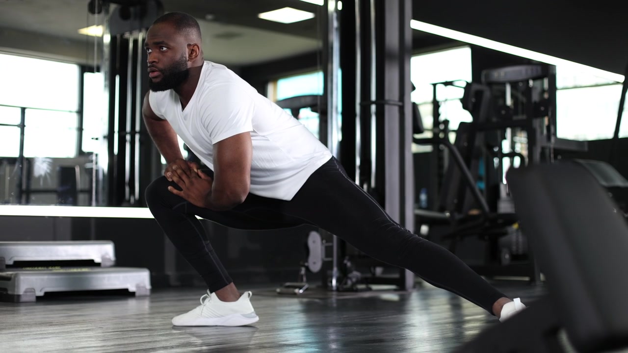 Athletic Man Performing Lunge Stretch in a Modern Gym