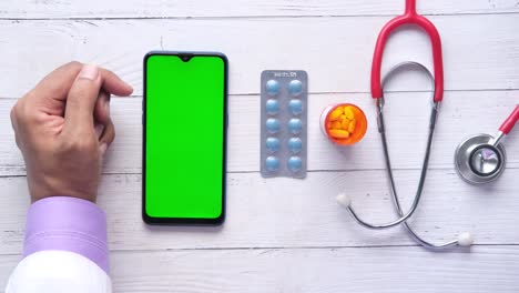 doctor using a smartphone with green screen for telemedicine consultation, showing medical equipment and pills