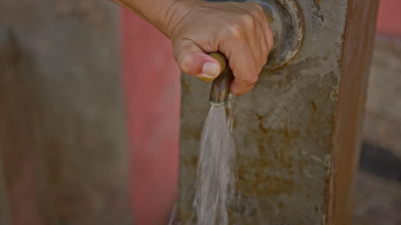 persona que usa un dispensador de agua al aire libre en una pared de piedra, vista de cerca