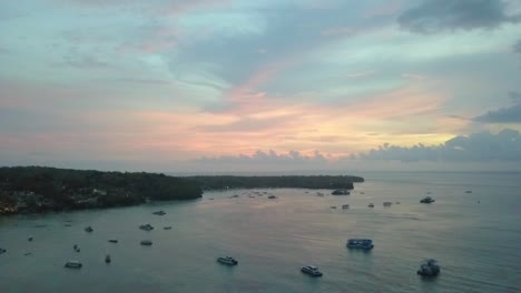 Sanfter-Luftbildflug-Rückwärts-Fliegende-Drohnenaufnahmen-Bei-Goldenem-Traumsonnenuntergang-Mit-Bunten-Wolken,-Die-Sich-In-Der-Mushroom-Bay-Lembongan-Spiegeln