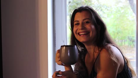 Hermosa-Mujer-Feliz-Con-Una-Taza-De-Café-Sentada-En-El-Alféizar-De-La-Ventana