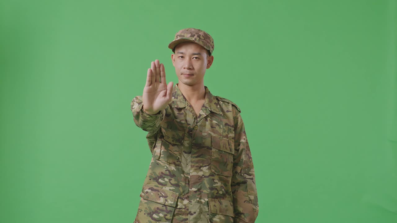Asian Man Soldier Looking At Camera And Disapproving With No Hand Sign While Standing In The Green Screen Background Studio