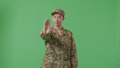 Asian Man Soldier Looking At Camera And Disapproving With No Hand Sign While Standing In The Green Screen Background Studio