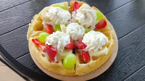 a waffle topped with strawberries, green grapes, and banana, drizzled with icing - zoom out shot