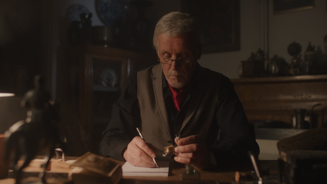 Older passionate man evaluates an old silver skull watch in his office at night