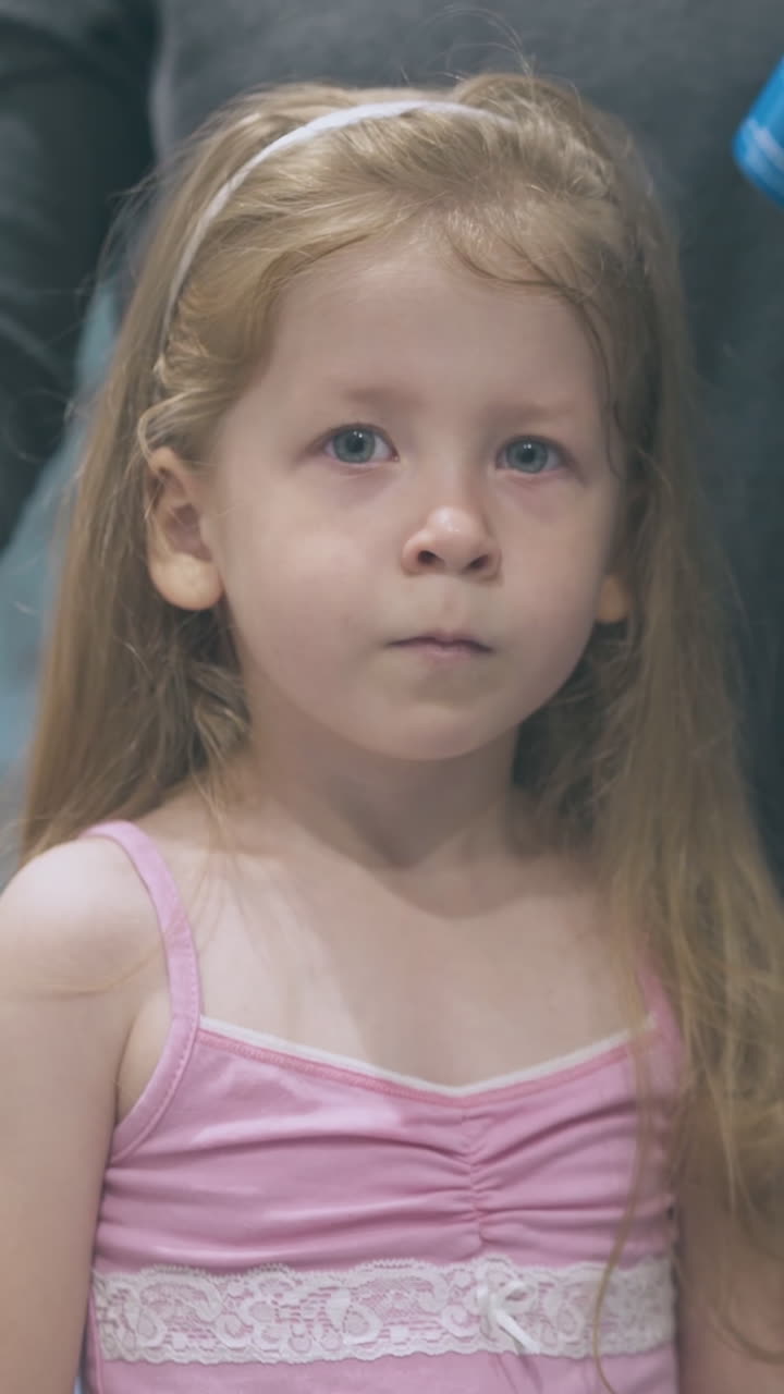 pretty little girl with long fair hair and careful mother with bottle for rinsing nose at mirror in bathroom at home