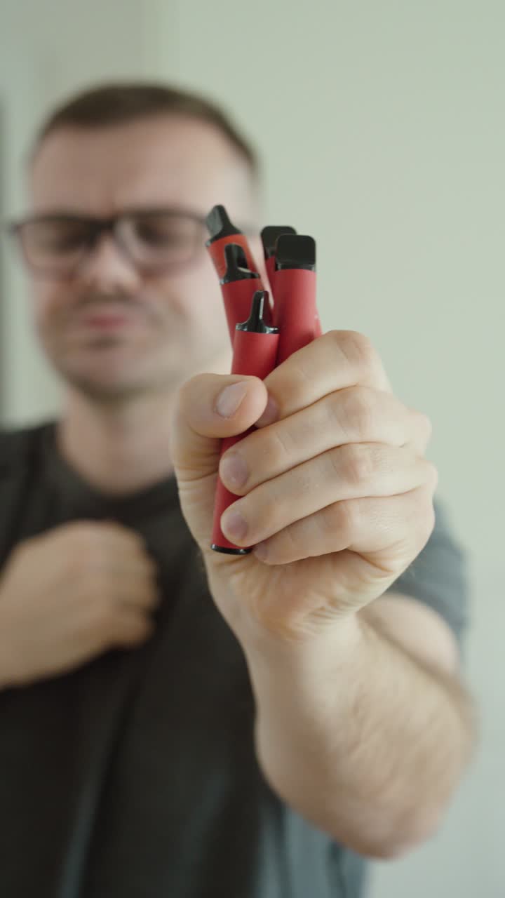 Primer plano de un hombre sosteniendo múltiples vapers desechables mientras tose, destacando los riesgos para la salud, la adicción y el impacto de los cigarrillos electrónicos. Ideal para temas antitabaco, concienciación sobre la salud y estilo de vida.