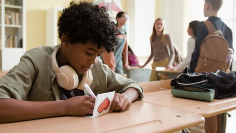 young student drawing a heart on a card in a classroom
