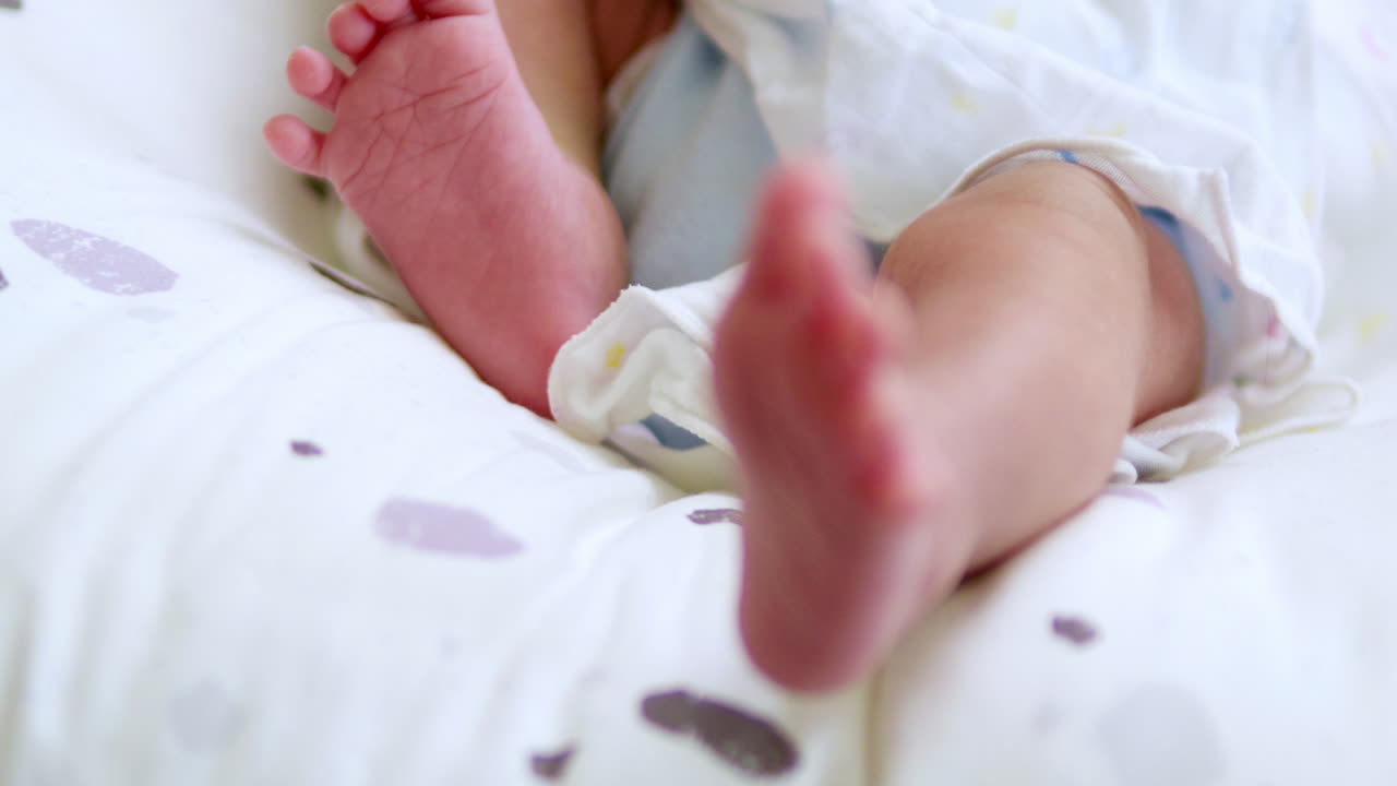 Primo piano di una neonata che allunga la gamba sinistra e poi contemporaneamente la gamba destra mentre è sdraiata sul letto