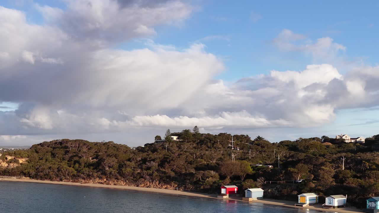 Camera pans across vibrant beach huts, coastal landscape, and dramatic sky in afternoon light