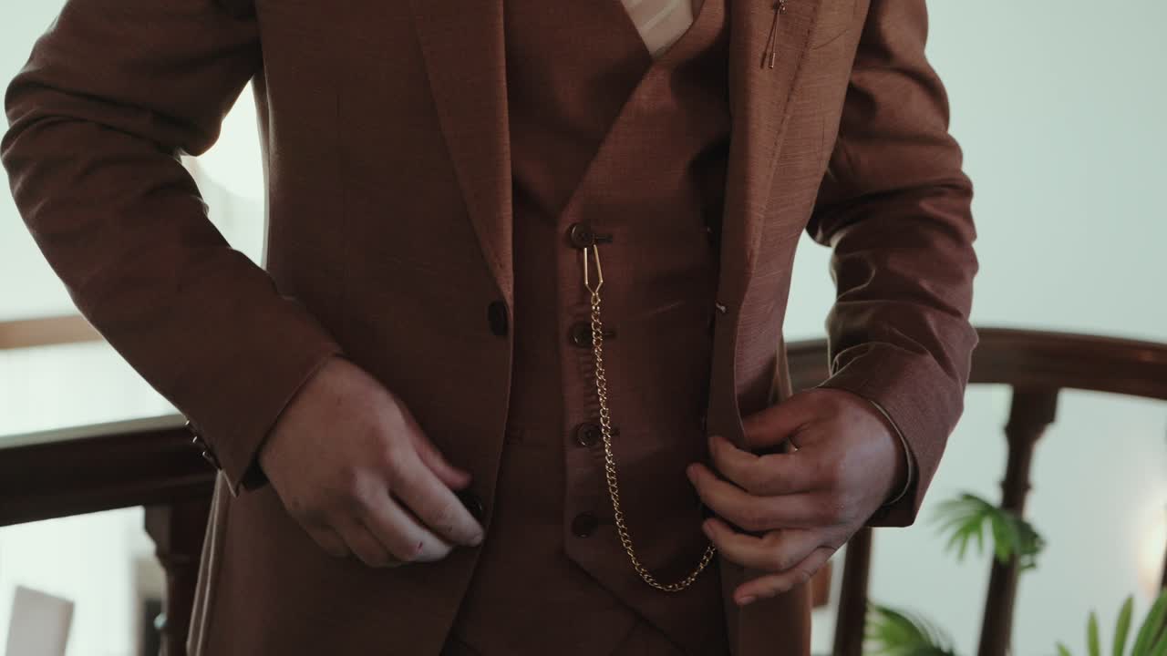 primer plano de unas manos abrochando un traje marrón con una cadena de reloj de bolsillo vintage