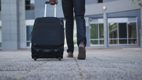 Low-section-of-african-american-businessman-walking-with-suitcase-in-street