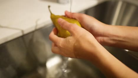 hands washing a pear under running water