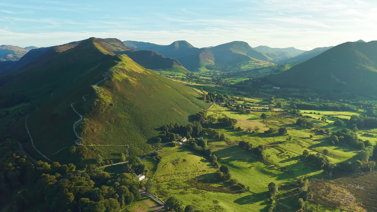 Golden hour light and long shadows over lush green farmland, Cat Bells and fells near Keswick