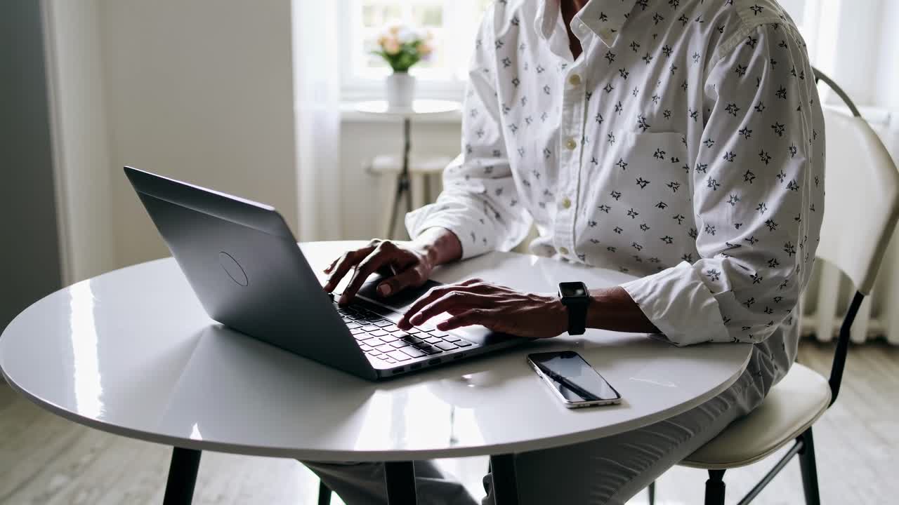A person types on a laptop at a round table, captured from a side angle