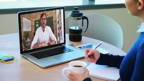 Caucasian-female-student-using-laptop-on-video-call-with-male-teacher,-making-notes