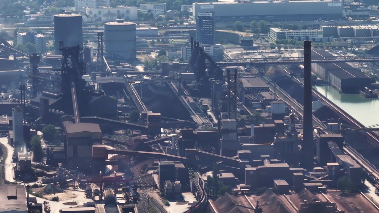 Expansive aerial view of a large steel plant and metallurgical industrial complex located on the banks of a river with smoke rising from chimneys