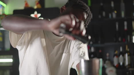 bartender pouring liquor into jigger at bar, preparing cocktail with focus on measuring, bartender in white shirt with blurred background of neon lights, bar shelf, and liquor bottles
