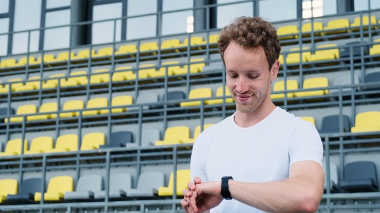 Uomo sportivo felice che controlla il suo smartwatch prima dell'allenamento all'aperto nello stadio 1