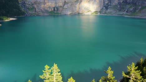 ascending revealing shot of oeschinen lake from behind sunlit trees in the swiss alps