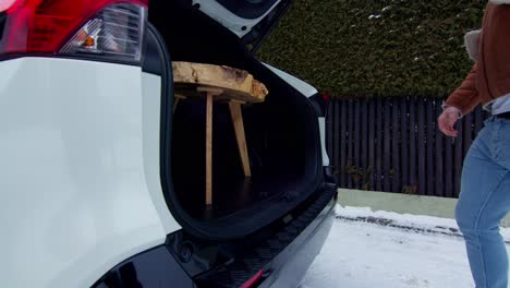 zoom in to a young man putting a small wooden table in the trunk of an off-road car