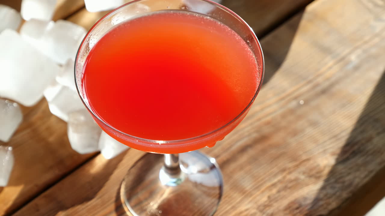 Mano che posiziona un cocktail rosso in un bicchiere a coppa su un tavolo di legno