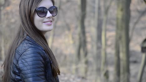 hermosa joven morena con gafas de sol negras sentada en un parque público sonriendo a la cámara en una bonita tarde de primavera