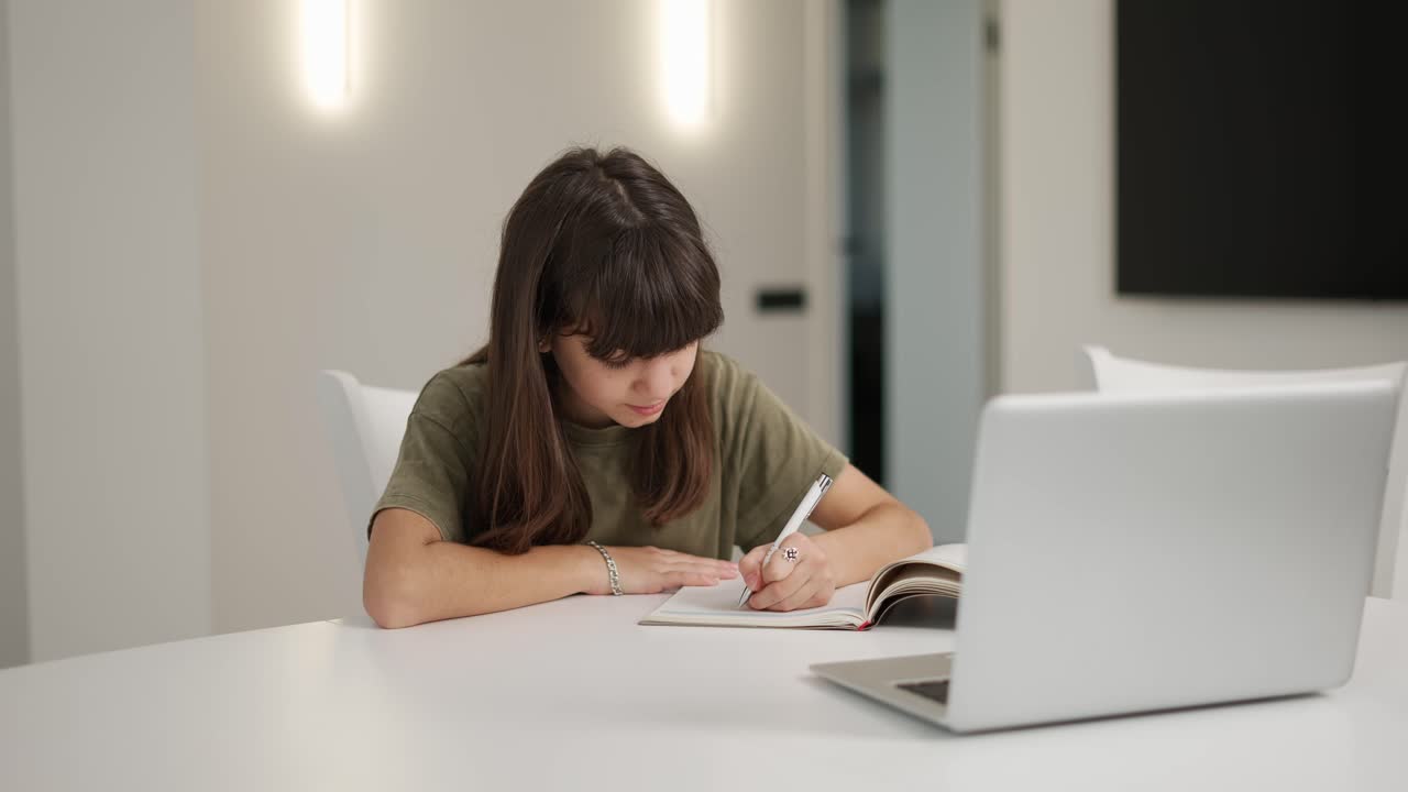 chica adolescente morena sentada en el escritorio haciendo su tarea usando una computadora portátil