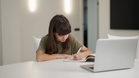 Brunette-teen-girl-sitting-at-the-desk-doing-her-homework-using-a-laptop