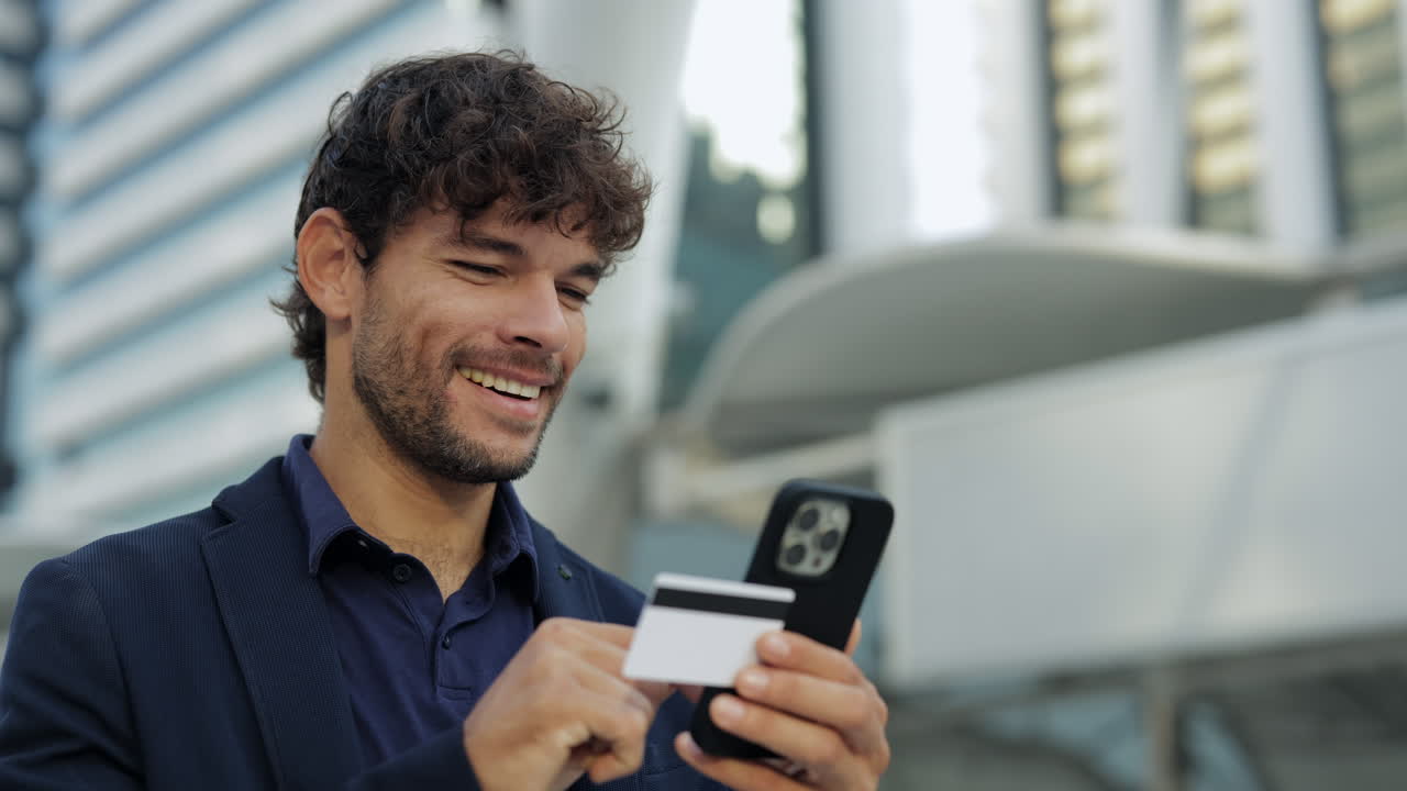 Hombre feliz haciendo un pago online con un smartphone y una tarjeta de crédito